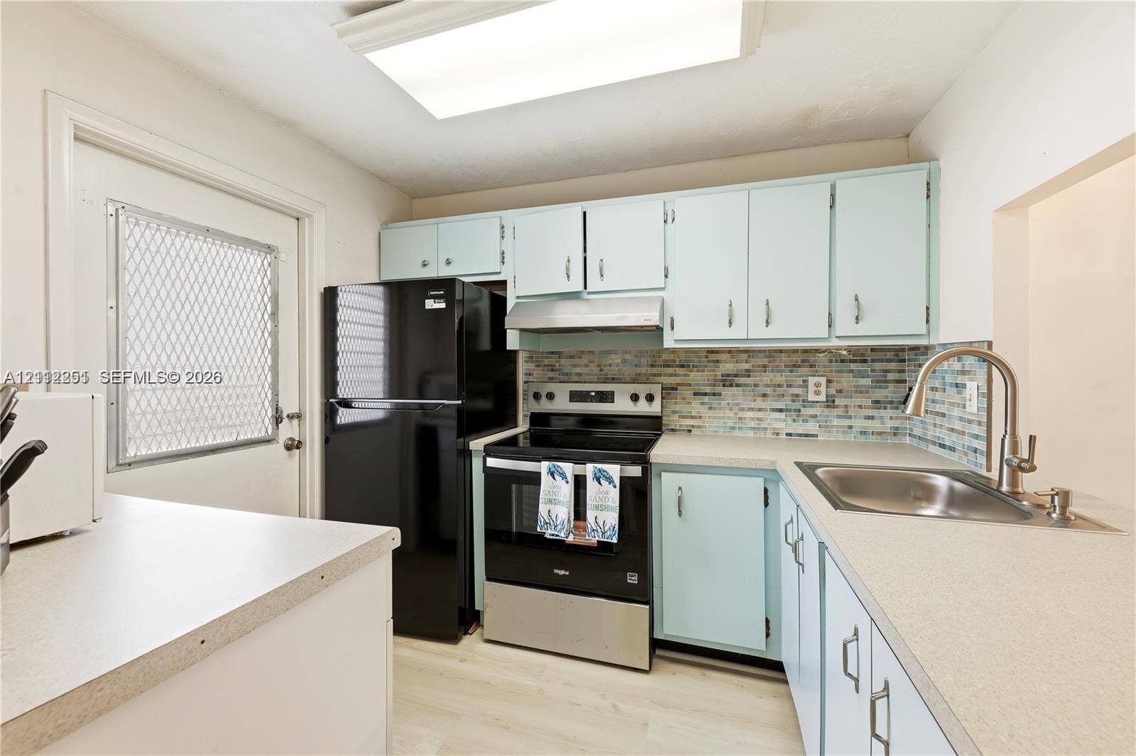4025 N Federal Highway, #226C, Oakland Park, FL 33308 Kitchen featuring pale blue cabinetry, solid surface countertops, multi-toned mosaic tile backsplash, stainless steel range with overhead hood, and light-tone wood-finish flooring