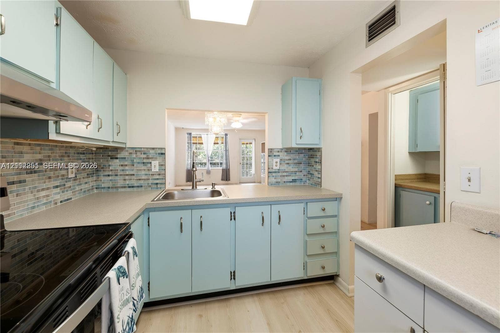 4025 N Federal Highway, #226C, Oakland Park, FL 33308 Kitchen featuring solid-surface countertops, custom light blue cabinetry, decorative glass tile backsplash, stainless steel sink, and wood-finish flooring