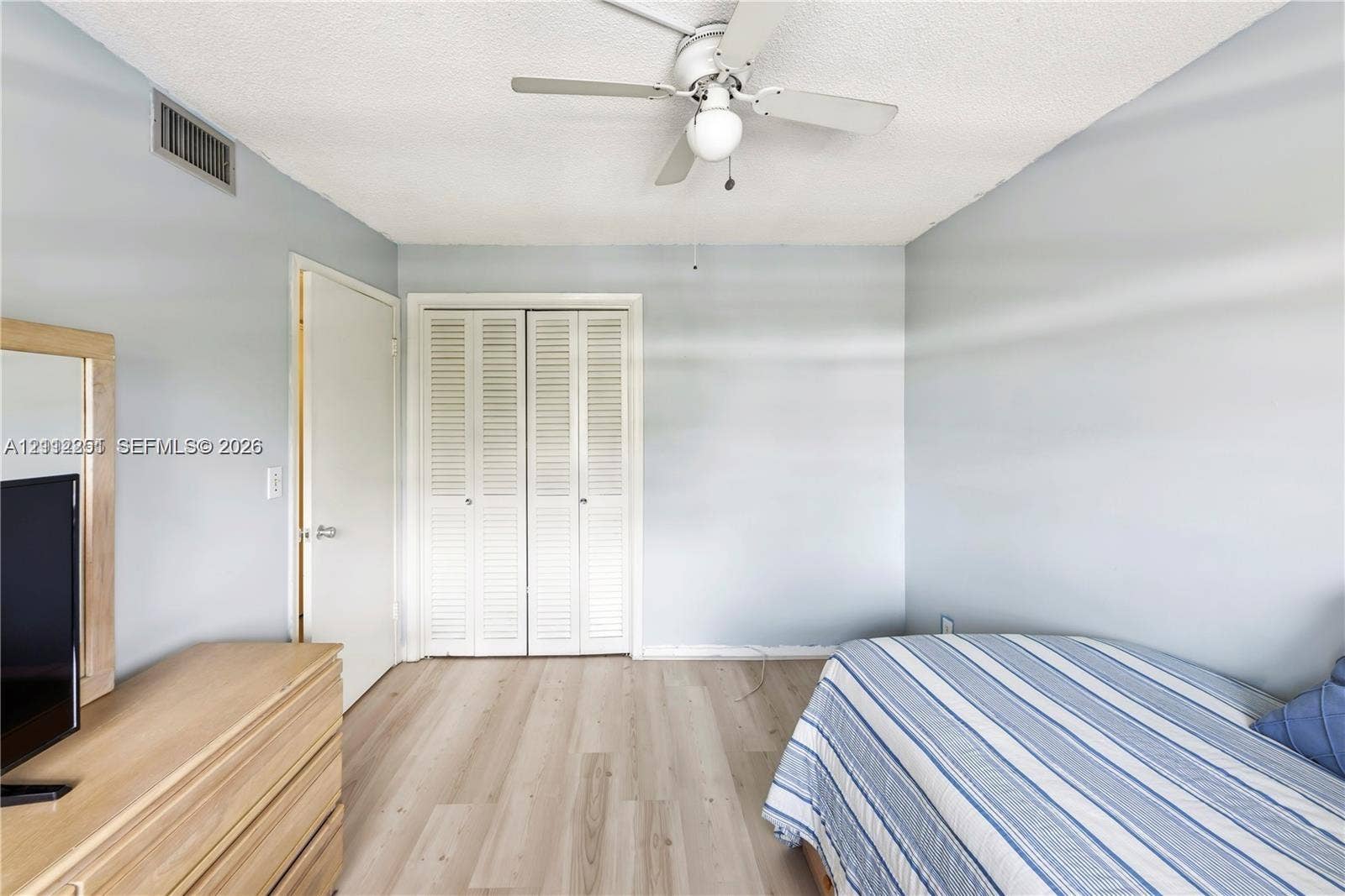 4025 N Federal Highway, #226C, Oakland Park, FL 33308 Room featuring wood-finish flooring, white louvered-style closet doors, and a ceiling-mounted light fixture with a central fan
