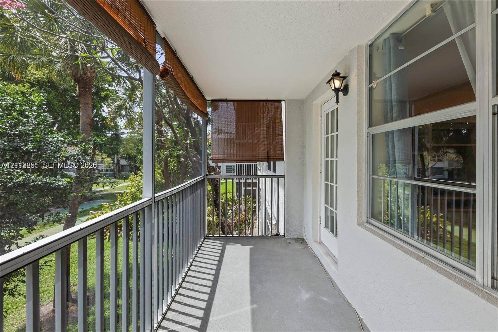 4025 N Federal Highway, #226C, Oakland Park, FL 33308 Screened balcony featuring vertical metal railings, concrete flooring, exterior wall-mounted lighting, and a glass-paneled entry door