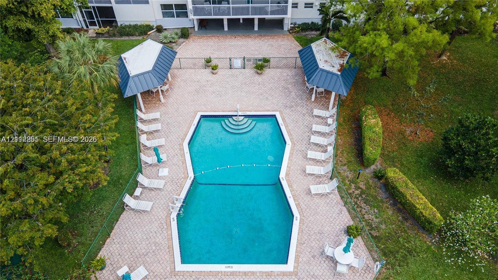 4025 N Federal Highway, #226C, Oakland Park, FL 33308 Swimming pool with built-in stairs, surrounded by a paved deck, two covered cabanas with metal roofing, and landscaped grounds