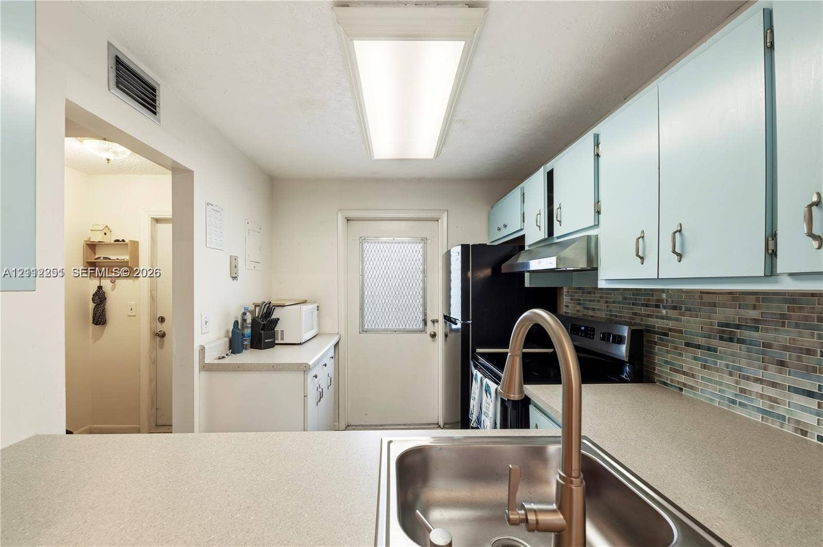 4025 N Federal Highway, #226C, Oakland Park, FL 33308 Kitchen featuring a stainless steel undermount sink, gooseneck faucet, solid-surface countertops, multicolored glass tile backsplash, and recessed panel cabinetry
