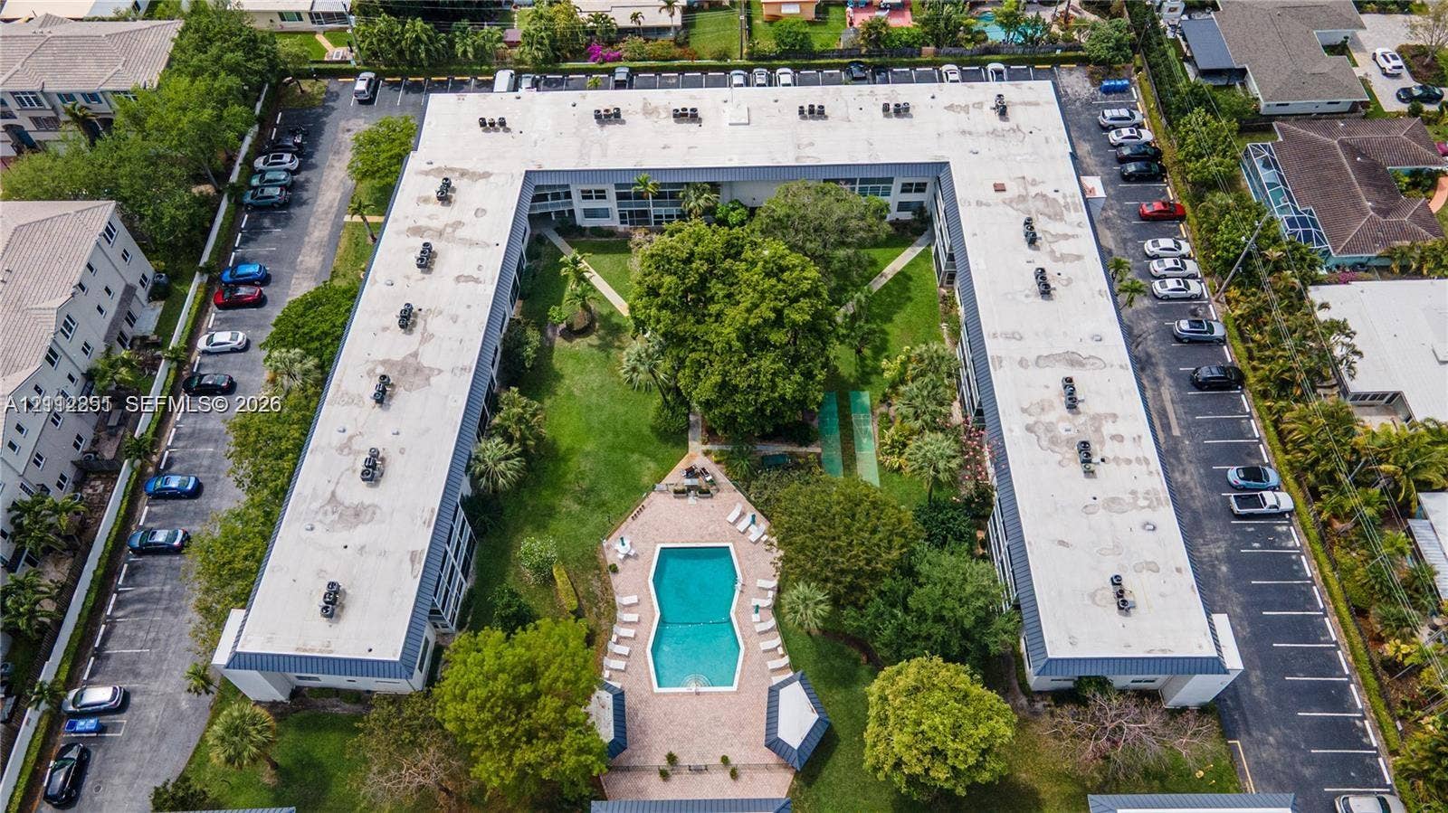 4025 N Federal Highway, #226C, Oakland Park, FL 33308 U-shaped residential complex featuring a central courtyard with a swimming pool, paver deck, mature landscaping, and dedicated surface parking