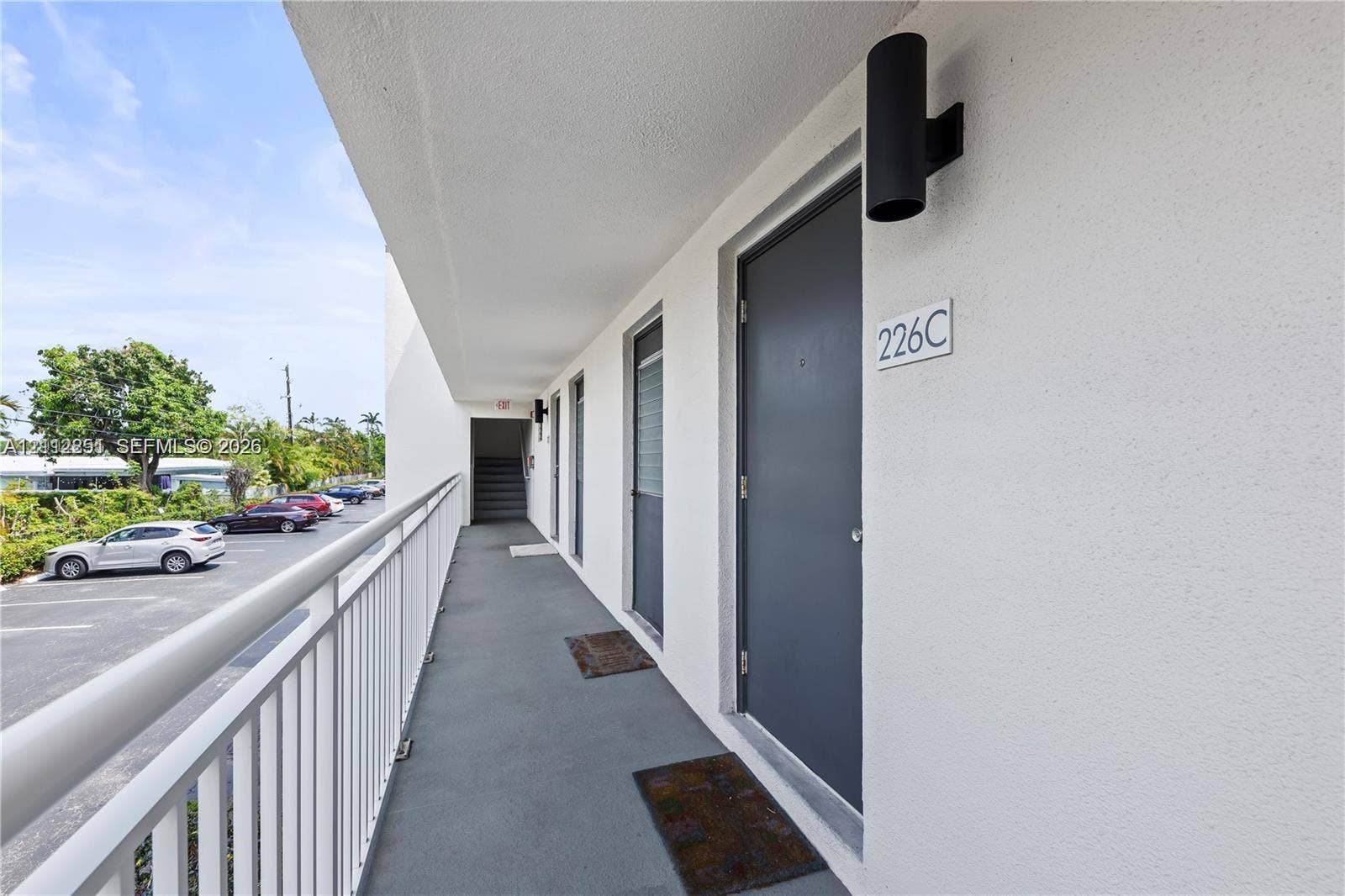 4025 N Federal Highway, #226C, Oakland Park, FL 33308 Exterior walkway featuring white stucco walls, grey entry doors, vertical matte black sconce lighting, and a white metal railing