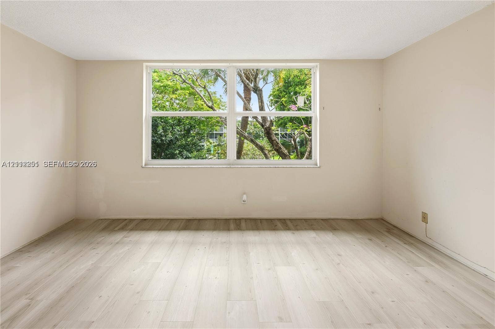 4025 N Federal Highway, #226C, Oakland Park, FL 33308 Room featuring wood-finish flooring, neutral-toned walls, and a large horizontal window with exterior greenery