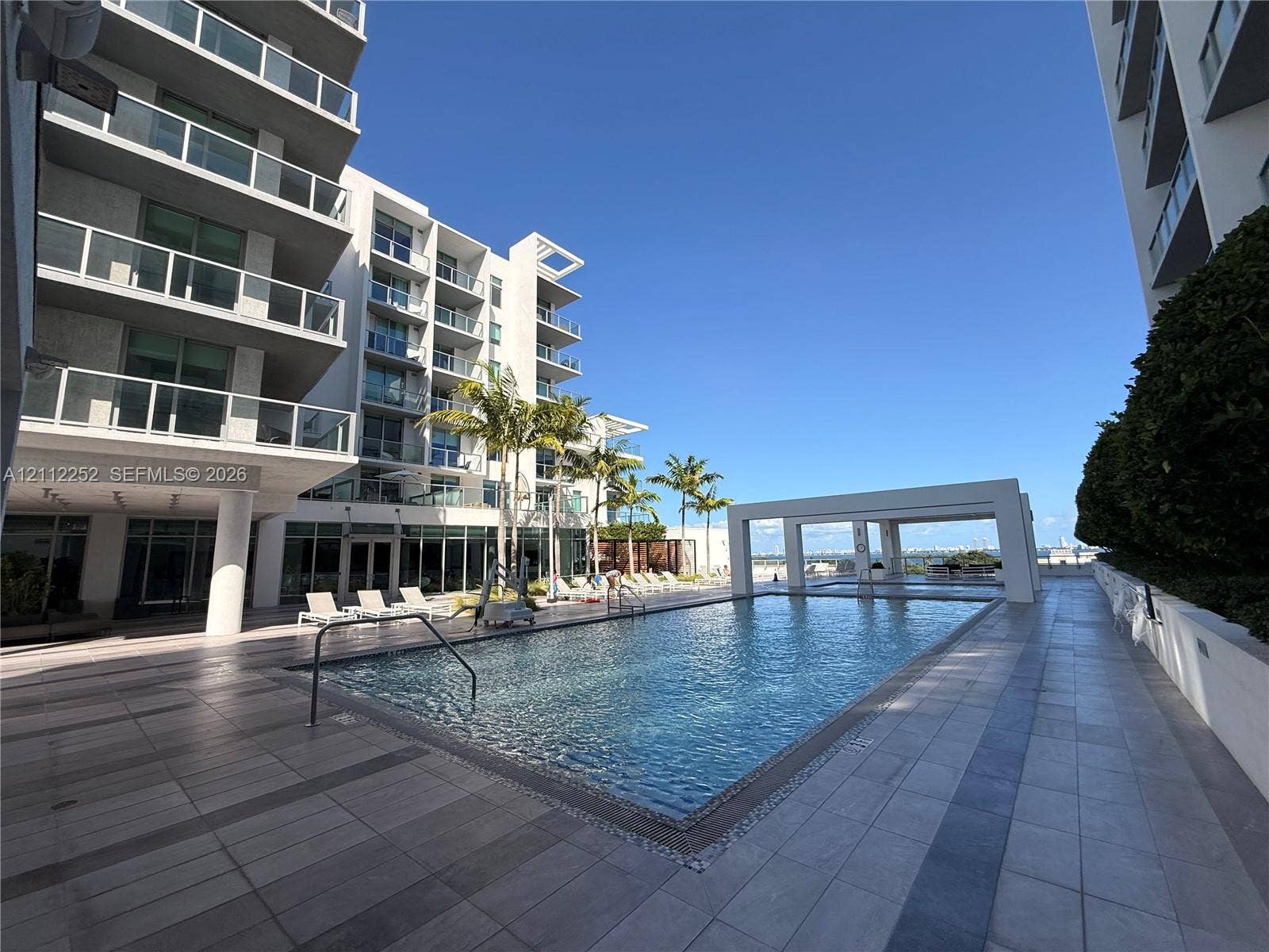 3900 Biscayne Boulevard, #N-1113, Miami, FL 33137 Swimming pool with tiled decking, poolside cabana, and multi-story architectural exterior featuring glass-paneled balconies