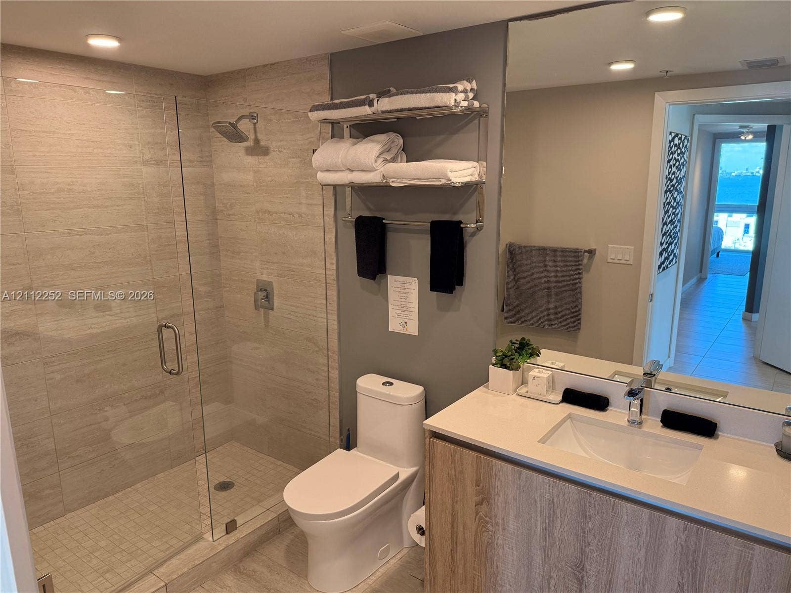 3900 Biscayne Boulevard, #N-1113, Miami, FL 33137 Walk-in shower with floor-to-ceiling stone-finish tile, vanity with wood-finish cabinetry, light-toned quartz countertop, integrated rectangular sink, and large wall-mounted mirror