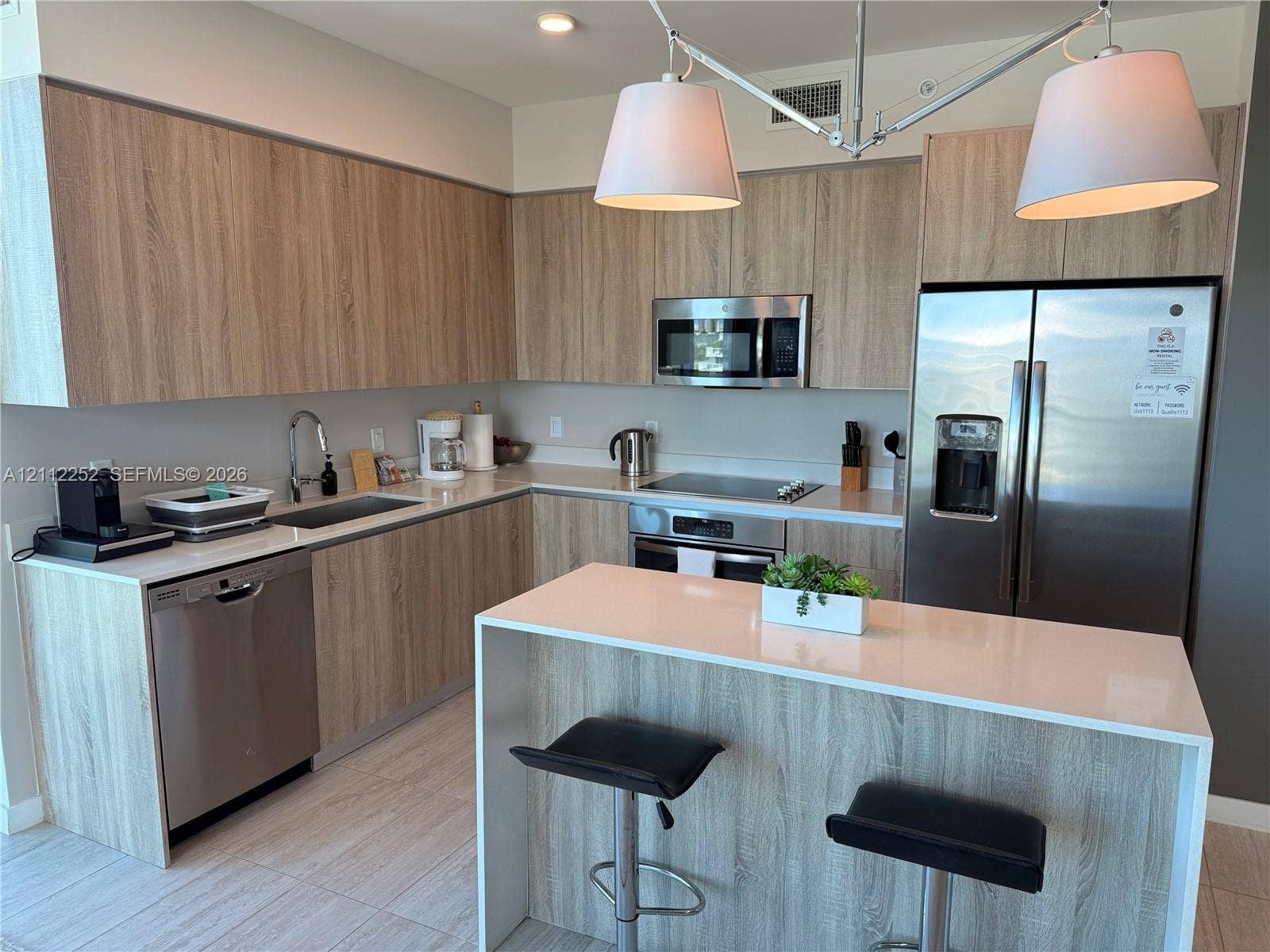 3900 Biscayne Boulevard, #N-1113, Miami, FL 33137 Kitchen featuring wood-finish cabinetry, white countertops, stainless steel appliances, and a waterfall-edge island with built-in seating