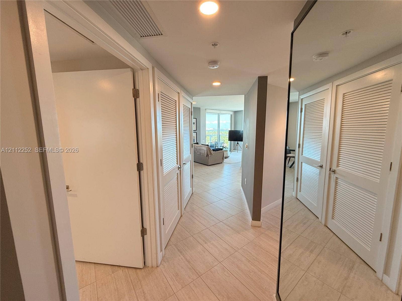 3900 Biscayne Boulevard, #N-1113, Miami, FL 33137 Hallway featuring large-format tile flooring, recessed ceiling lighting, louvered-panel closet doors, and a full-length mirrored door