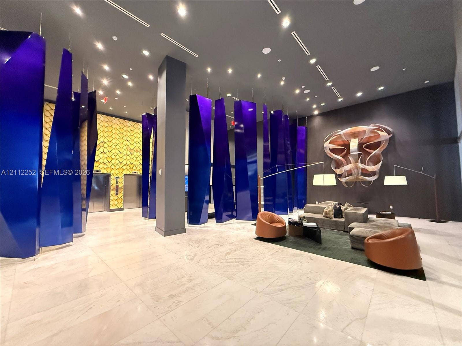3900 Biscayne Boulevard, #N-1113, Miami, FL 33137 Lobby featuring polished stone flooring, custom blue geometric architectural panels, recessed lighting, and intricate metallic wall-mounted sculpture