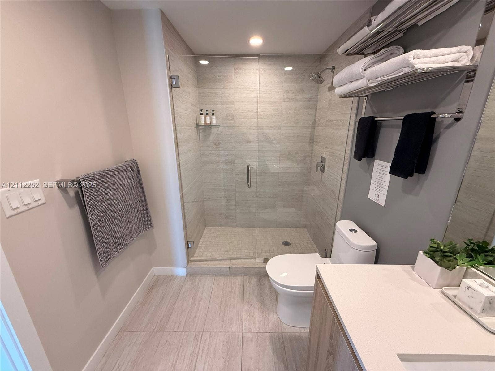 3900 Biscayne Boulevard, #N-1113, Miami, FL 33137 Walk-in shower with frameless glass enclosure, floor-to-ceiling stone-style wall tile, built-in shower niche, light-toned stone-style floor tile, and vanity with solid-surface countertop
