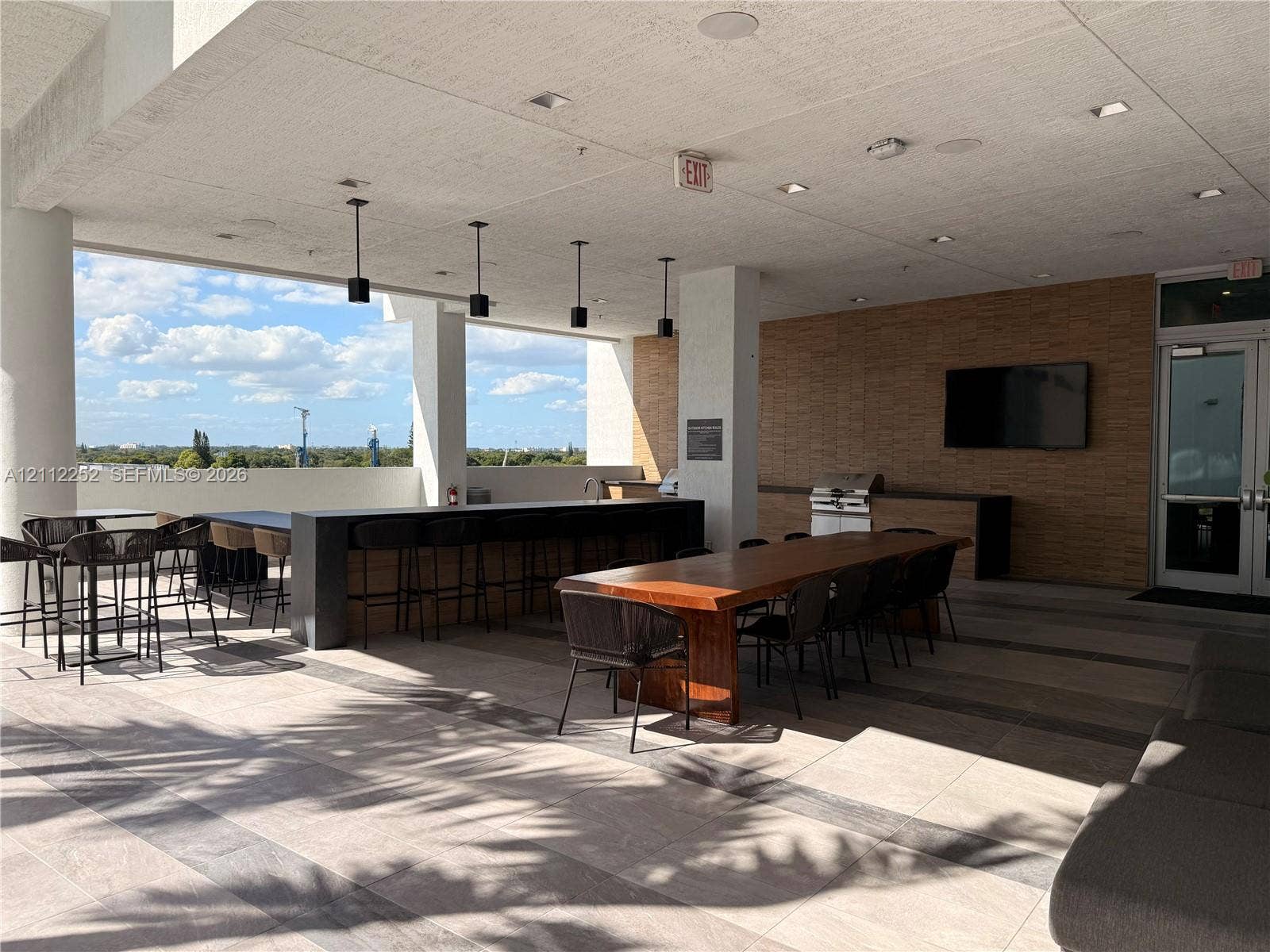 3900 Biscayne Boulevard, #N-1113, Miami, FL 33137 Covered rooftop terrace featuring large-format tile flooring, a built-in outdoor kitchen with stainless steel grill, a stone-tiled accent wall, and recessed ceiling lighting
