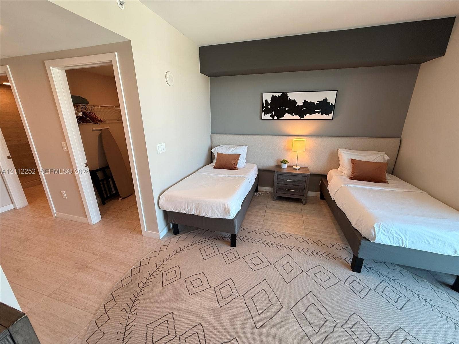 3900 Biscayne Boulevard, #N-1113, Miami, FL 33137 Neutral-toned interior featuring continuous light-colored flooring, a custom upholstered headboard wall, an accent wall with architectural bulkhead, and an open-entry reach-in closet with wire shelving
