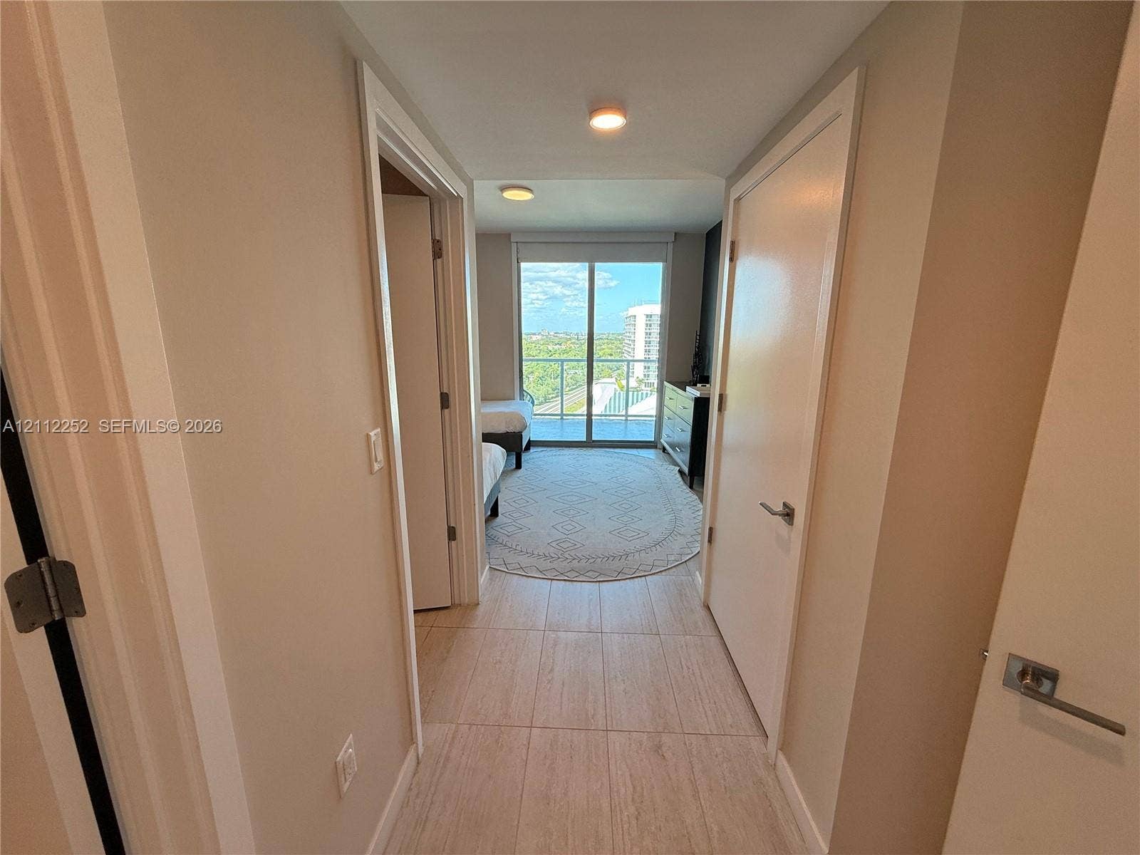 3900 Biscayne Boulevard, #N-1113, Miami, FL 33137 Hallway featuring large-format tile flooring and multiple interior doors, leading to a room with a floor-to-ceiling glass sliding door opening to an exterior balcony