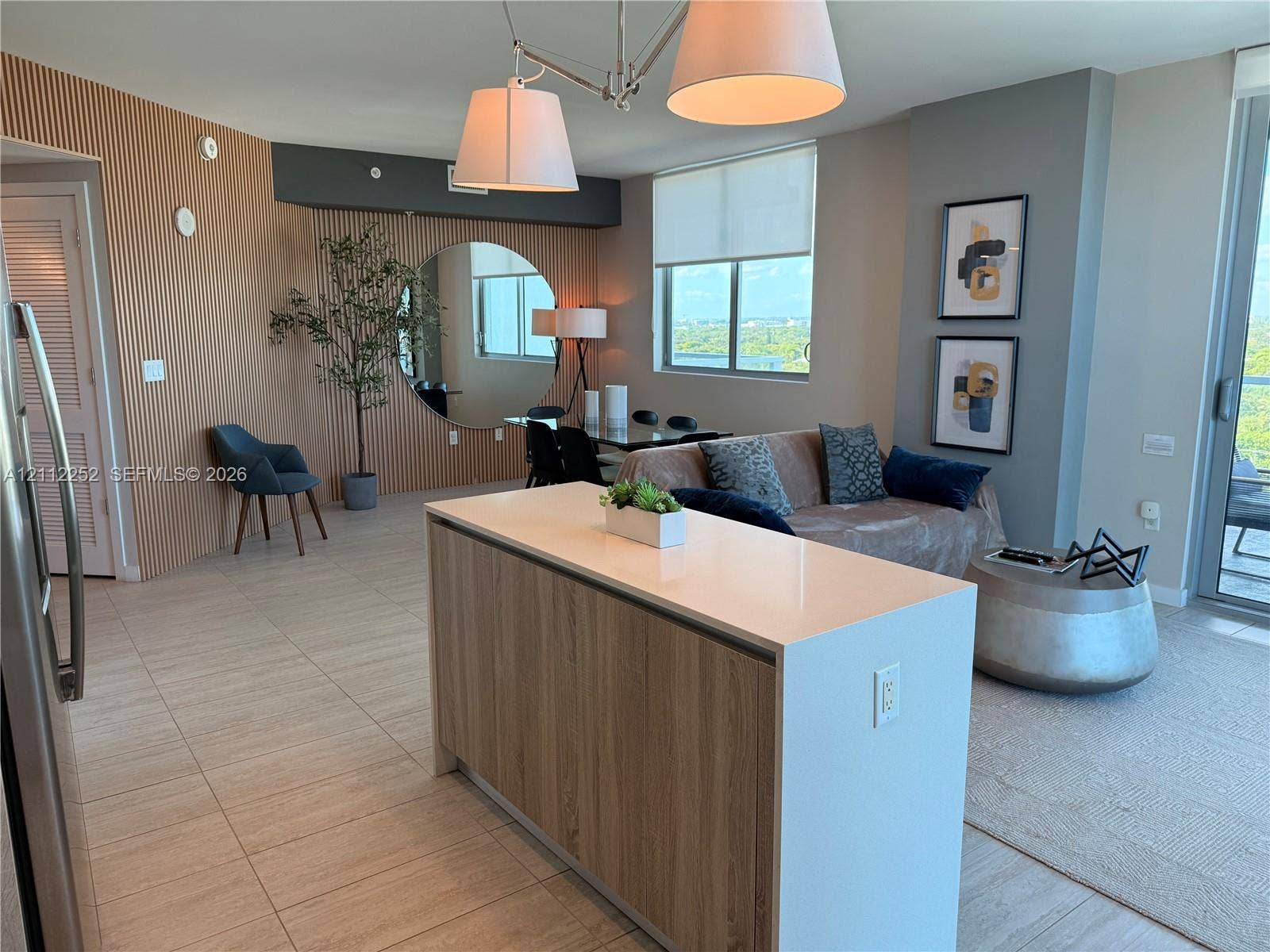 3900 Biscayne Boulevard, #N-1113, Miami, FL 33137 Kitchen island featuring a stone countertop and wood-finish cabinetry, accent wall with vertical fluting, large circular wall-mounted mirror, and tile flooring