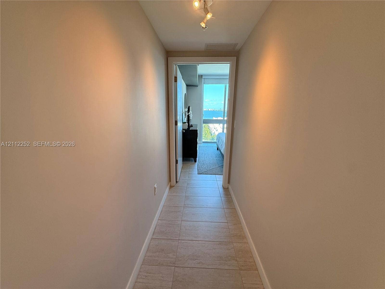 3900 Biscayne Boulevard, #N-1113, Miami, FL 33137 Hallway featuring neutral wall tones, tile flooring, and multi-directional track lighting, leading toward an exterior window