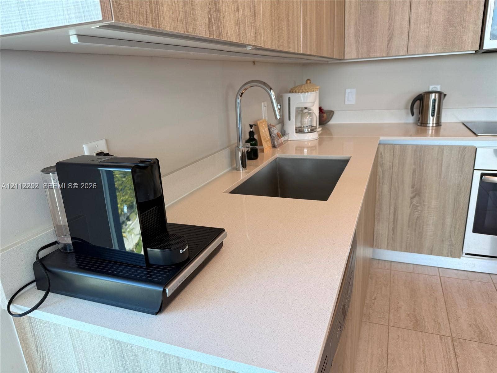 3900 Biscayne Boulevard, #N-1113, Miami, FL 33137 Kitchen featuring light wood-finish cabinetry, solid-surface countertops, an undermount stainless steel sink with a high-arch faucet, and an integrated oven