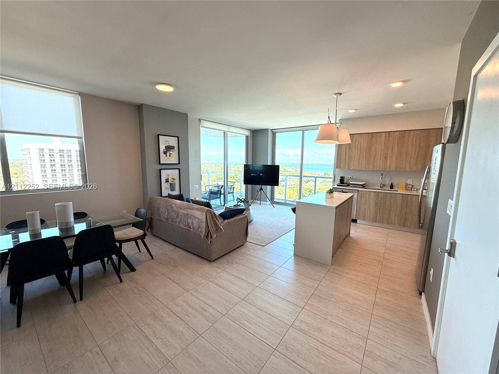 3900 Biscayne Boulevard, #N-1113, Miami, FL 33137 Open-concept living space featuring wood-finish cabinetry, a kitchen island, floor-to-ceiling glass windows, and ceramic tile flooring