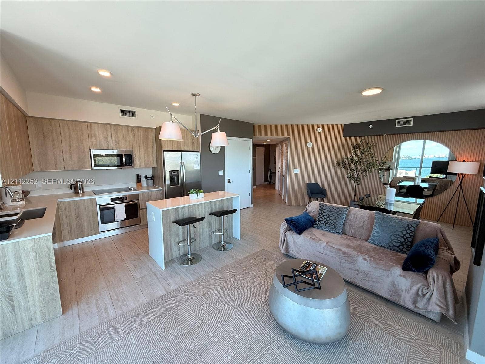 3900 Biscayne Boulevard, #N-1113, Miami, FL 33137 Open-concept kitchen featuring light wood-finish cabinetry, a central island with counter seating, stainless steel appliances, and wood-finish flooring throughout