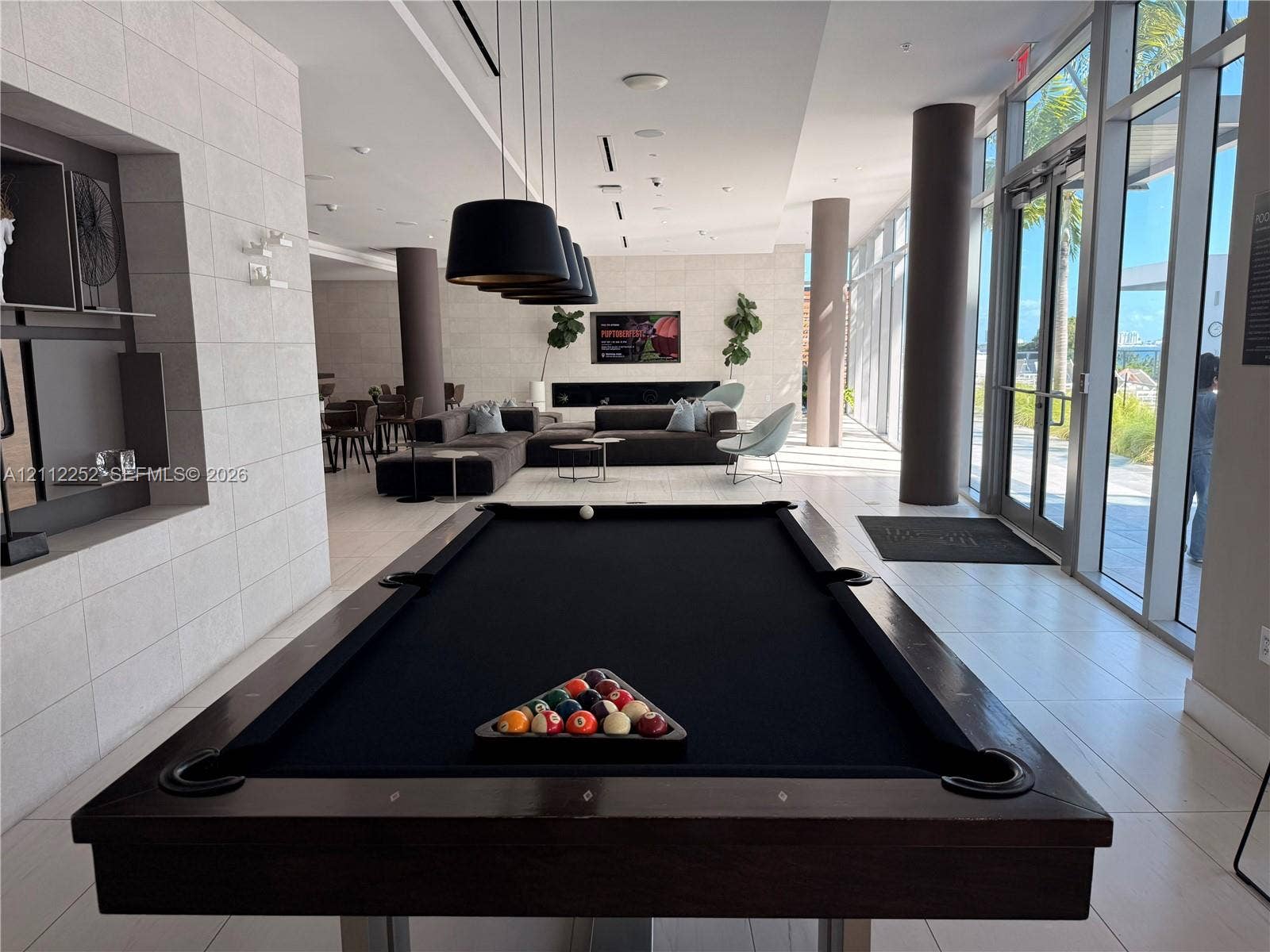 3900 Biscayne Boulevard, #N-1113, Miami, FL 33137 Common area featuring large-format tile flooring, floor-to-ceiling glass wall panels, built-in recessed shelving, matte black pendant lighting, and a linear fireplace