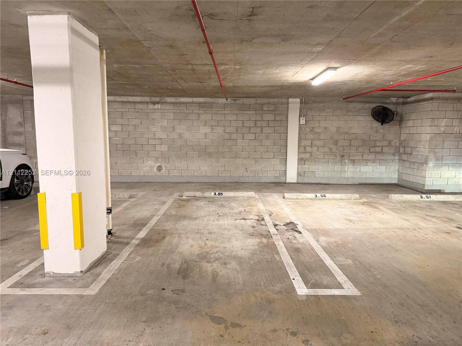 3900 Biscayne Boulevard, #N-1113, Miami, FL 33137 Covered parking area featuring concrete flooring, concrete block walls, painted support pillars with protective guards, and overhead lighting