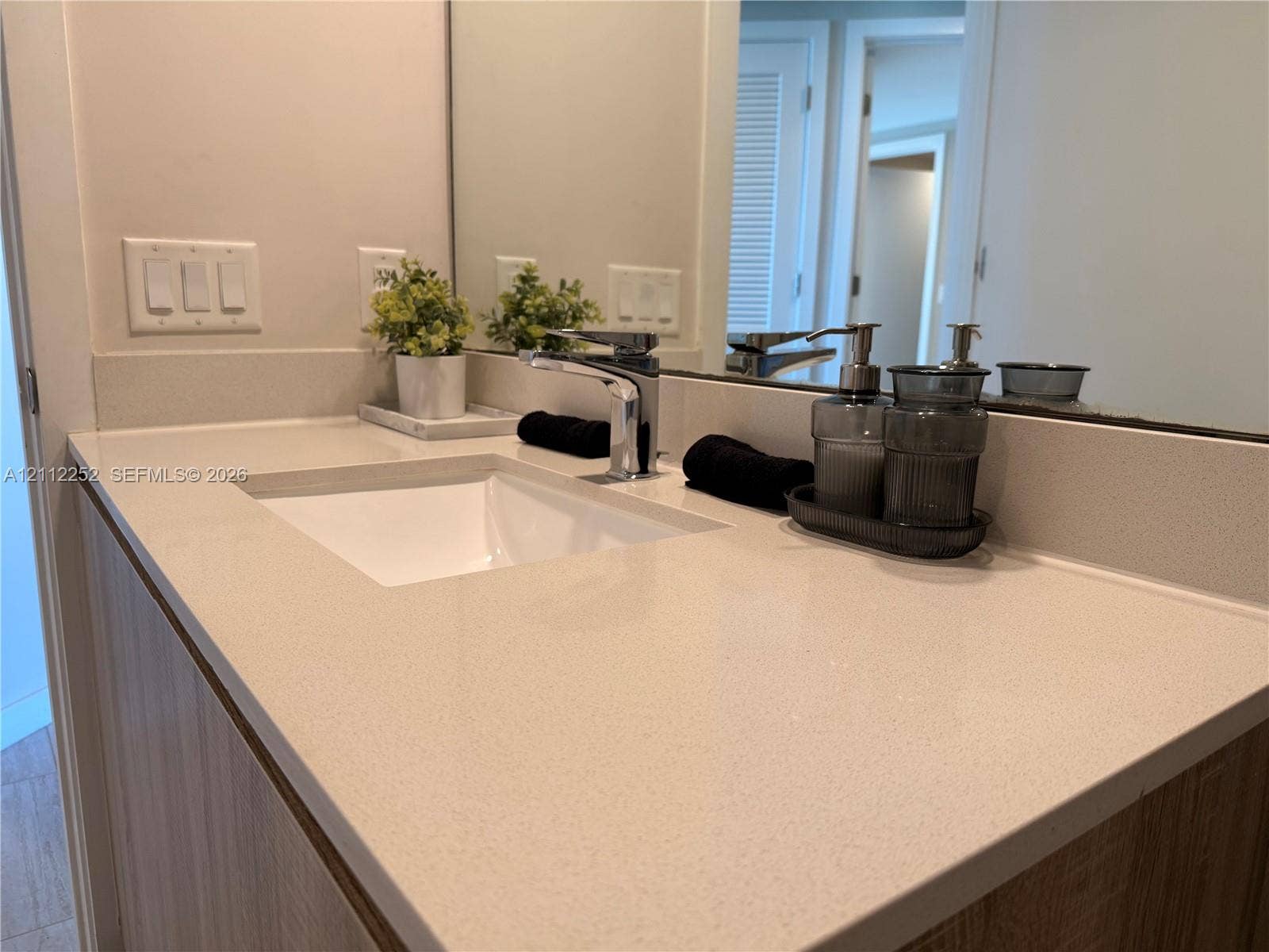 3900 Biscayne Boulevard, #N-1113, Miami, FL 33137 Vanity featuring a light-toned solid surface countertop, an integrated rectangular sink, a polished chrome faucet, and wood-finish cabinetry with a full-width mirror