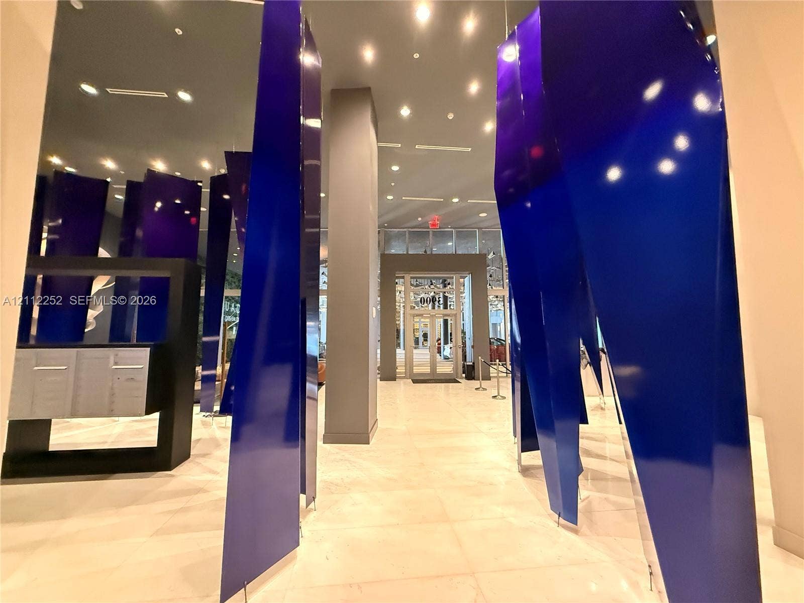 3900 Biscayne Boulevard, #N-1113, Miami, FL 33137 Grand lobby entrance featuring high-gloss geometric blue panels, large-format tile flooring, recessed ceiling lighting, and built-in metallic mailboxes