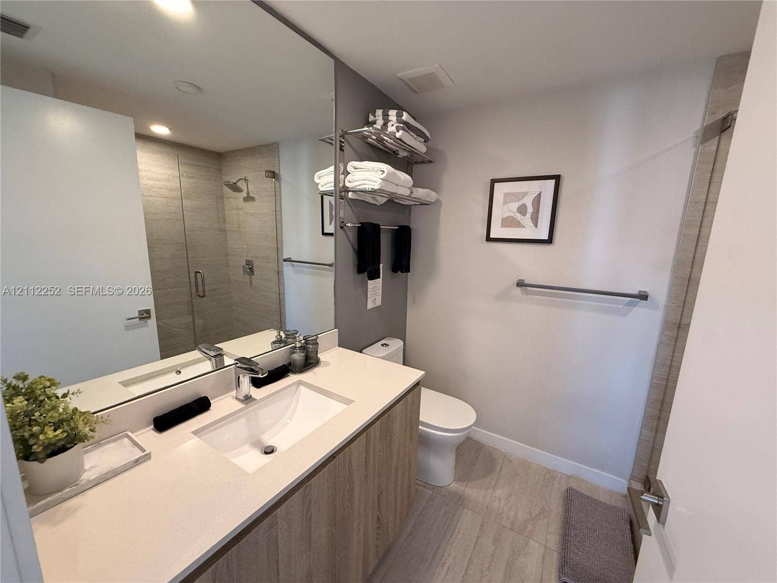 3900 Biscayne Boulevard, #N-1113, Miami, FL 33137 Bathroom featuring a vanity with a light-toned countertop, integrated basin, wood-finish cabinetry, floor-to-ceiling mirror, and a walk-in shower with horizontal-tiled walls and a glass enclosure