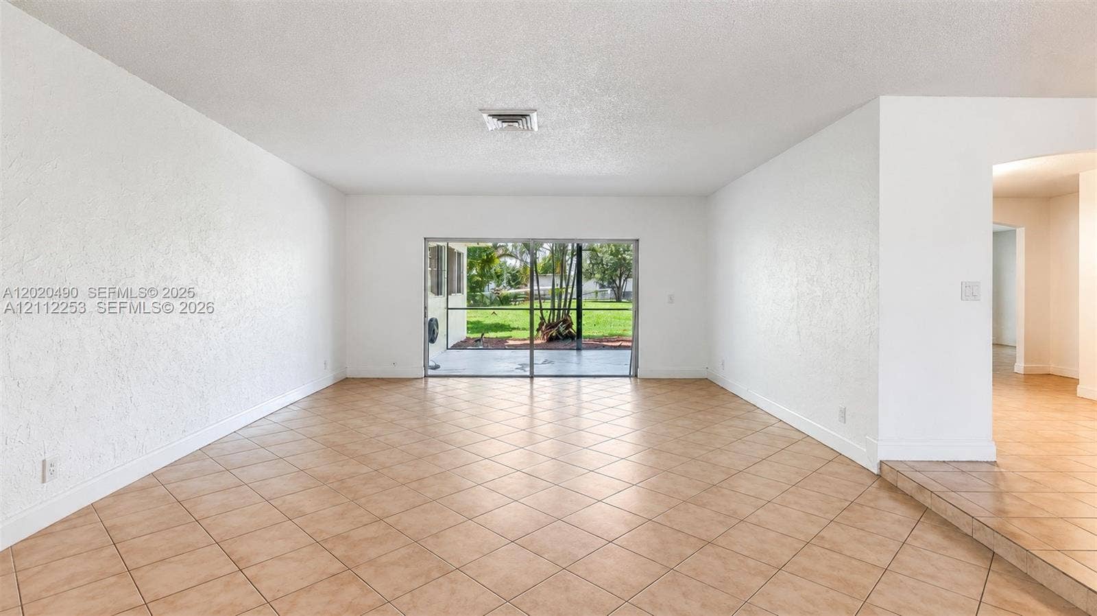 500 NW 96th Terrace, Pembroke Pines, FL 33024 Spacious interior featuring neutral tile flooring, textured wall finishes, and large sliding glass doors opening to a screened outdoor area