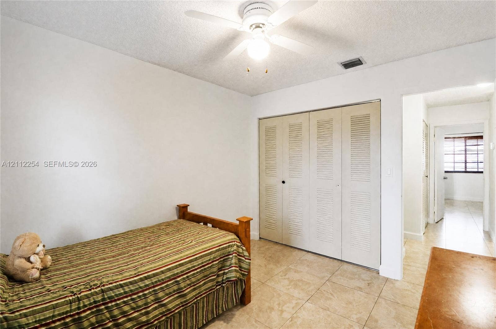 Neutral-toned tile flooring, three-panel louvered closet doors, and a ceiling fan with integrated lighting fixture