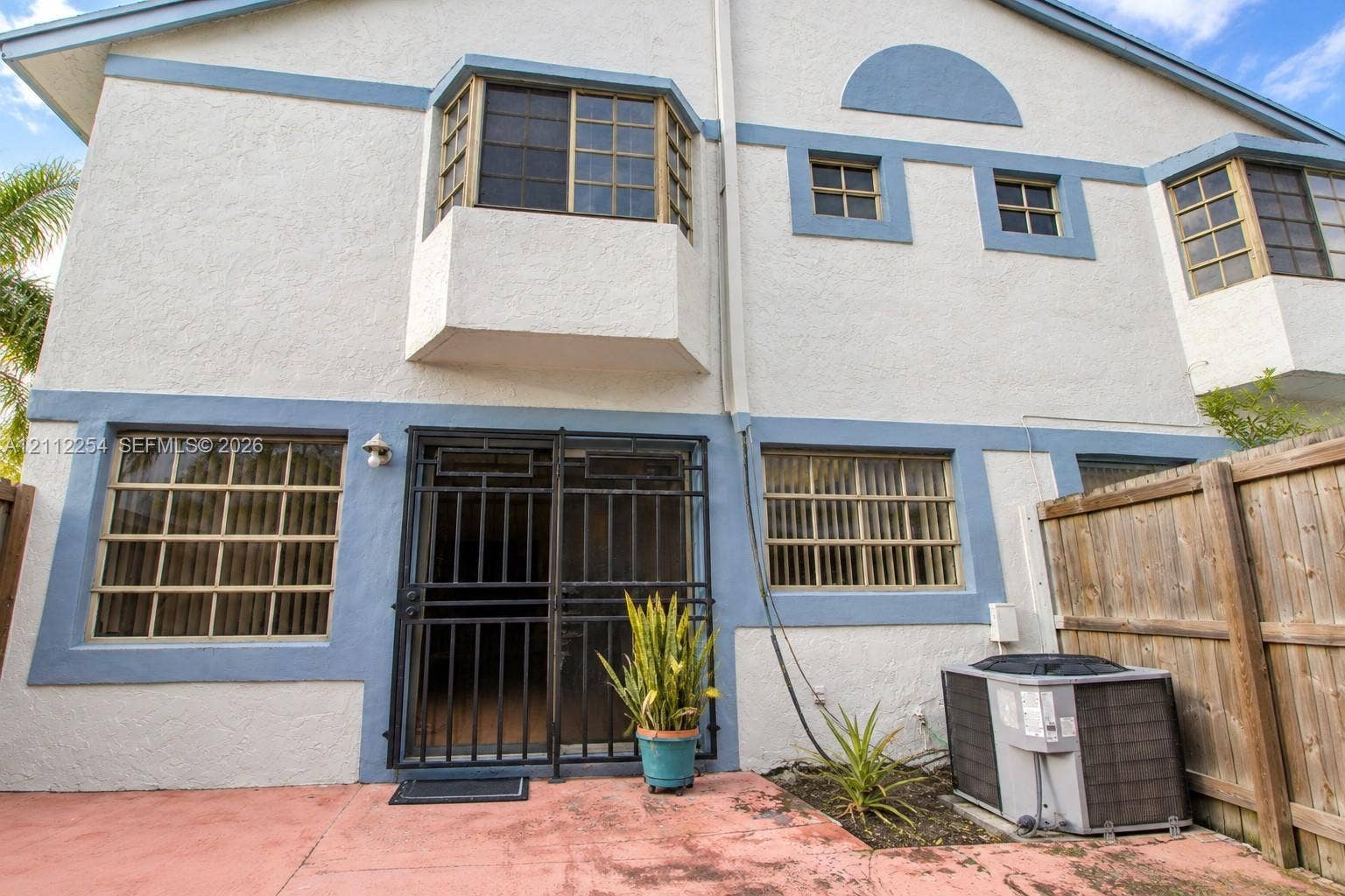 Stucco exterior with multi-level bay windows, grid-patterned glass, integrated security screen door, and exterior heating and cooling unit