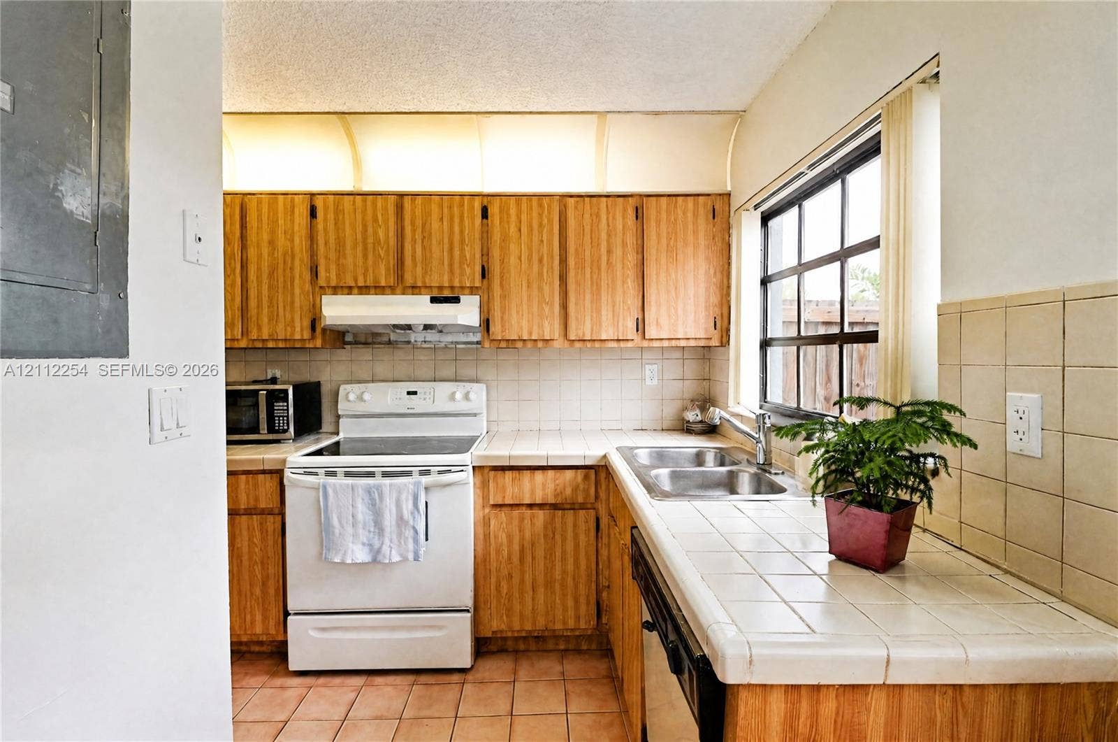 Kitchen featuring wooden cabinetry, white appliance suite, tiled countertops, and a grid-style window
