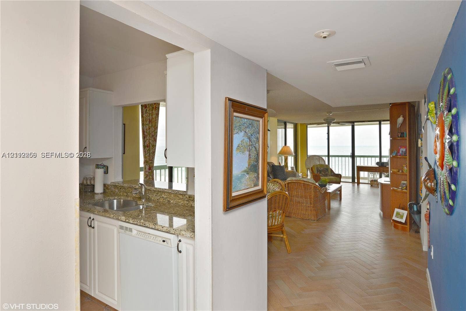 9900 S Ocean Drive, #601, Jensen Beach, FL 34957 Kitchen featuring white cabinetry, stone countertops, and an integrated stainless steel sink, paired with herringbone-patterned flooring
