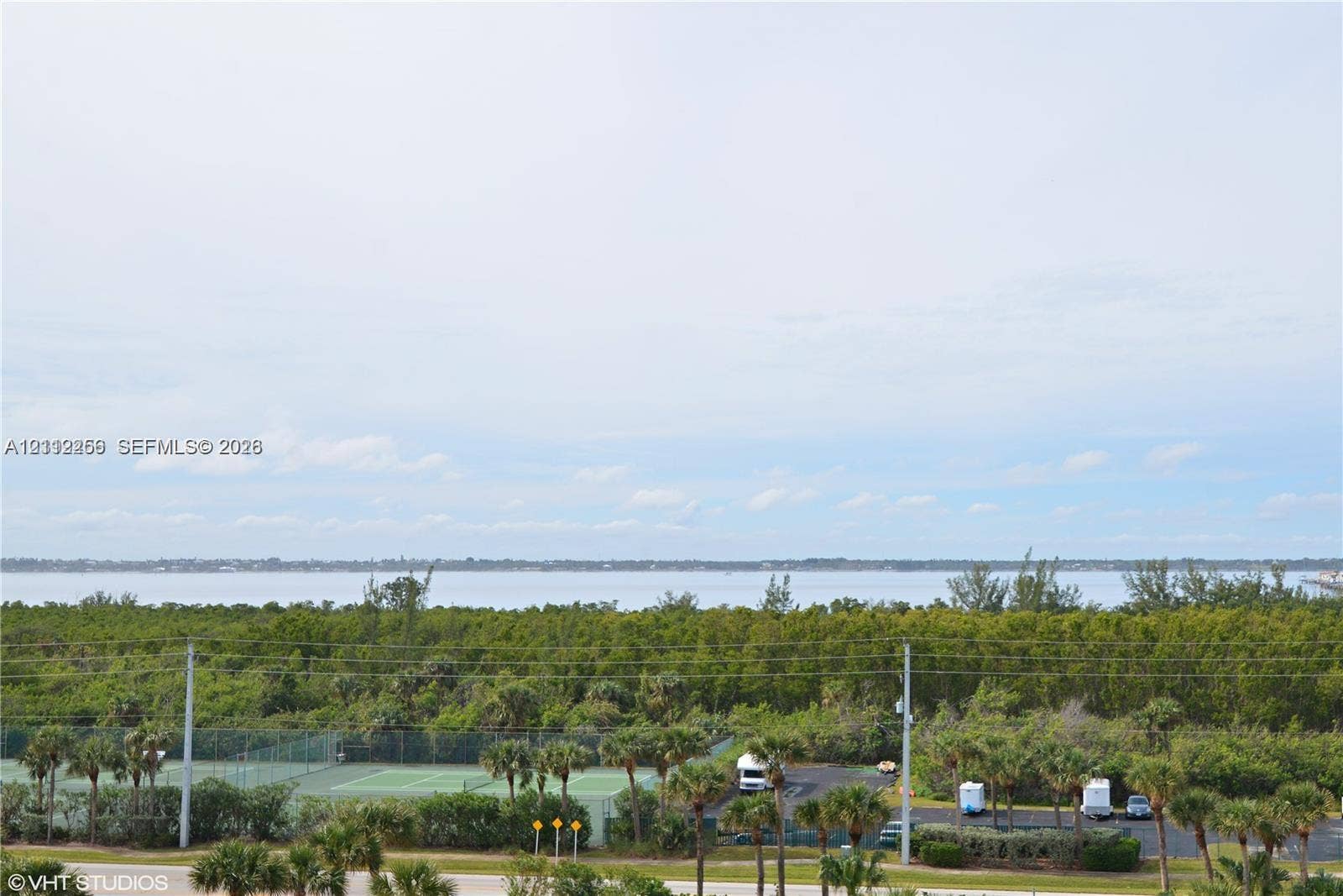 9900 S Ocean Drive, #601, Jensen Beach, FL 34957 Expansive water horizon with mature treeline, featuring an outdoor tennis court and paved parking area