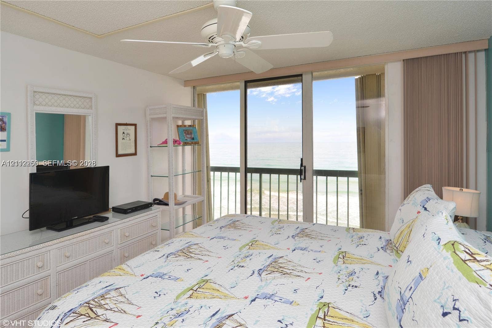 9900 S Ocean Drive, #601, Jensen Beach, FL 34957 Sliding glass doors opening to a balcony with metal railings and ocean water backdrop, ceiling fan, and wall-mounted mirror