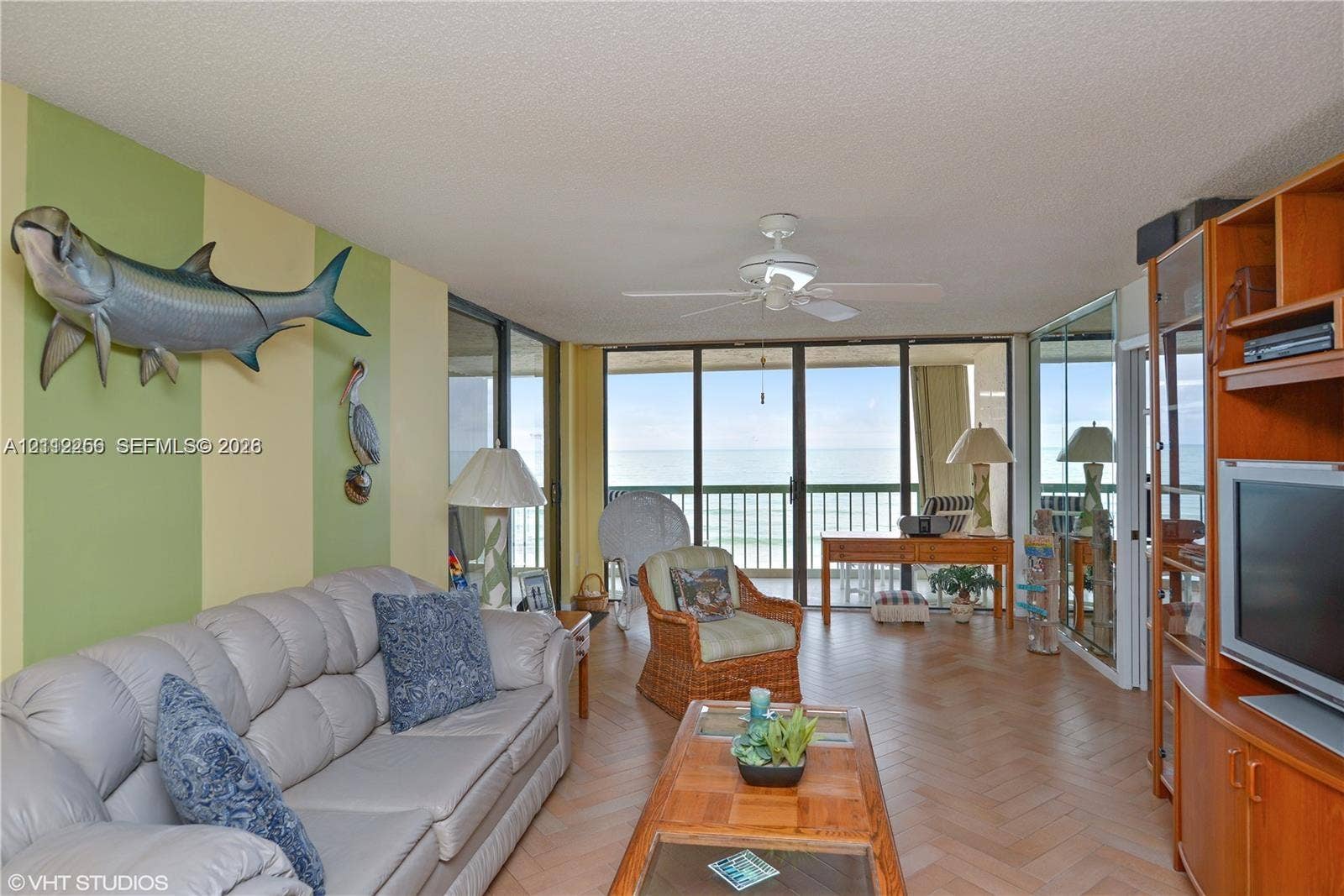 9900 S Ocean Drive, #601, Jensen Beach, FL 34957 Living space featuring herringbone-patterned wood-finish flooring, floor-to-ceiling glass sliding doors, integrated mirrored wall panels, and a ceiling fan