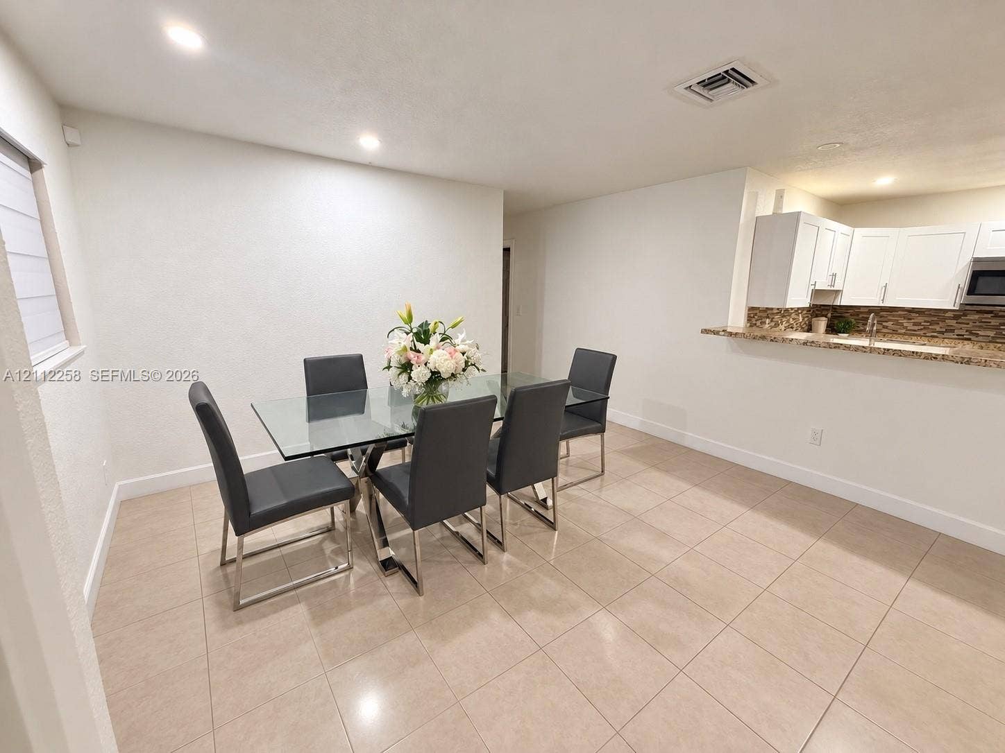 Open-concept space featuring large-format neutral floor tile, white shaker-style cabinetry, a stone-patterned backsplash, and a breakfast bar