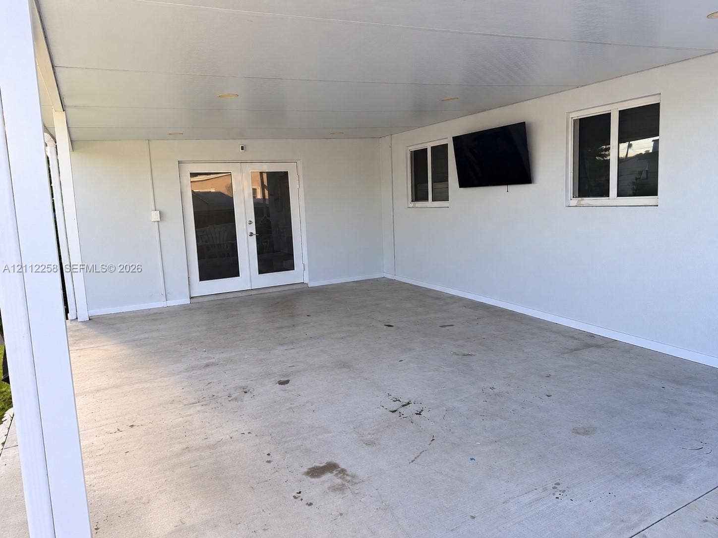 Covered patio featuring a concrete floor, recessed ceiling lighting, wall-mounted television, and glass-paneled double doors