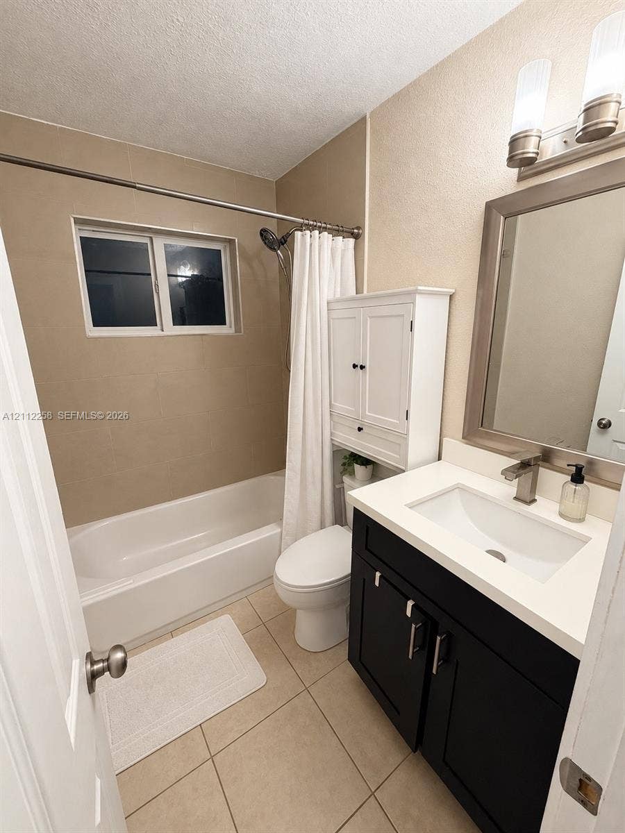 Bathroom featuring a dark-finish vanity with a white countertop and rectangular undermount sink, wall-mounted white cabinetry, tile flooring, and a shower-tub combination with tile surround