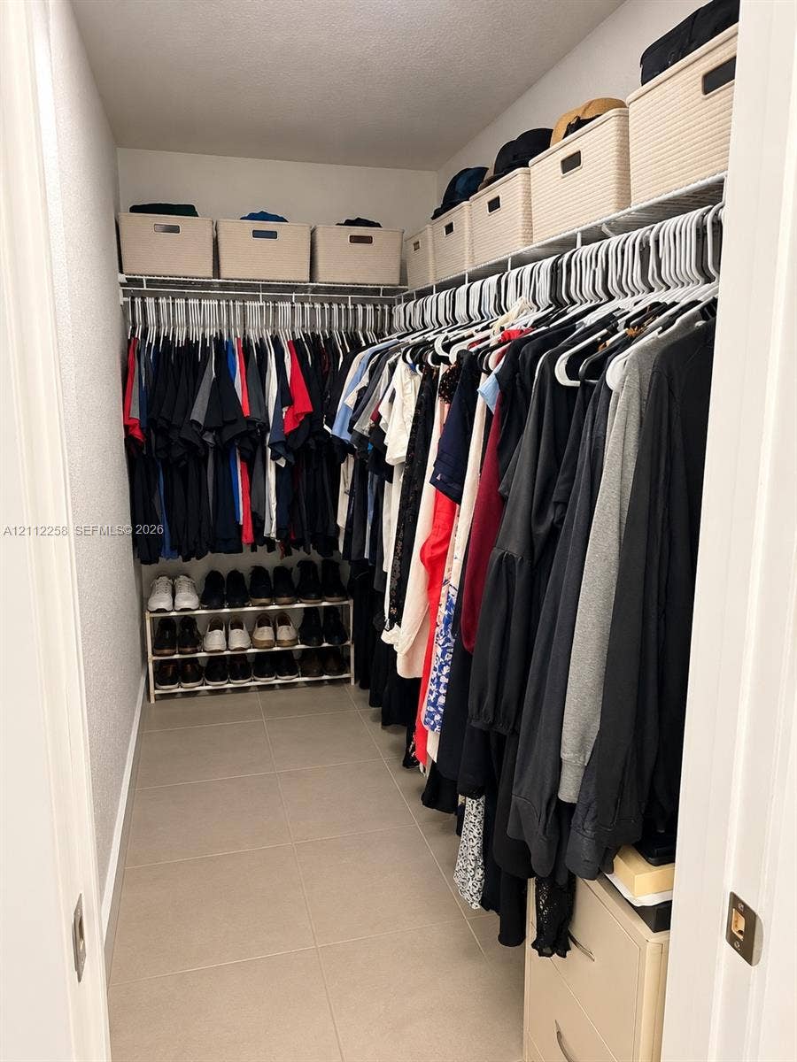 Walk-in closet featuring floor-to-ceiling wire shelving, tile flooring, and integrated lower cabinetry