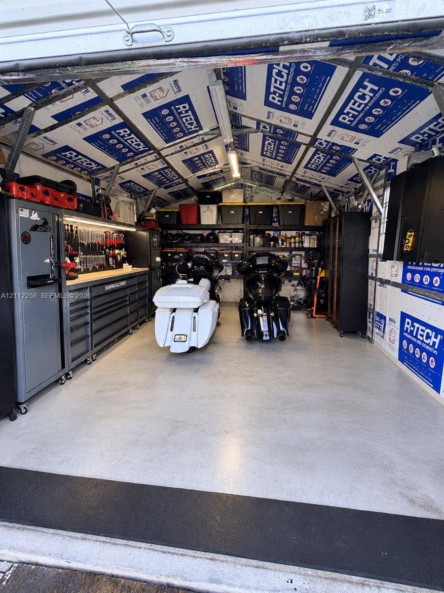 Workshop area featuring high-density foam insulation panels, epoxy-coated flooring, built-in metal cabinetry, overhead LED tube lighting, and heavy-duty adjustable shelving units