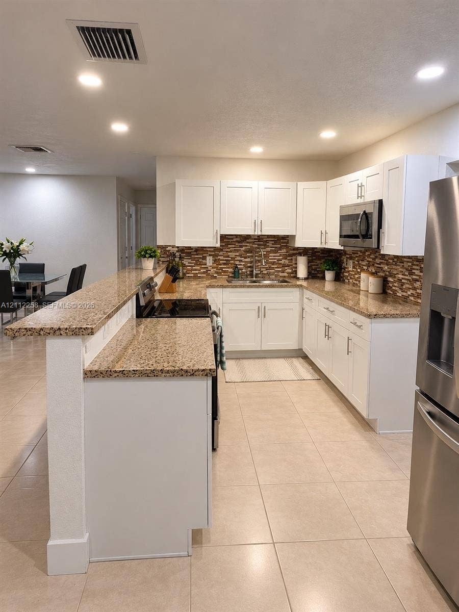 Kitchen featuring white shaker-style cabinetry, stone-finish countertops, tile backsplash, stainless steel appliances, and tile flooring