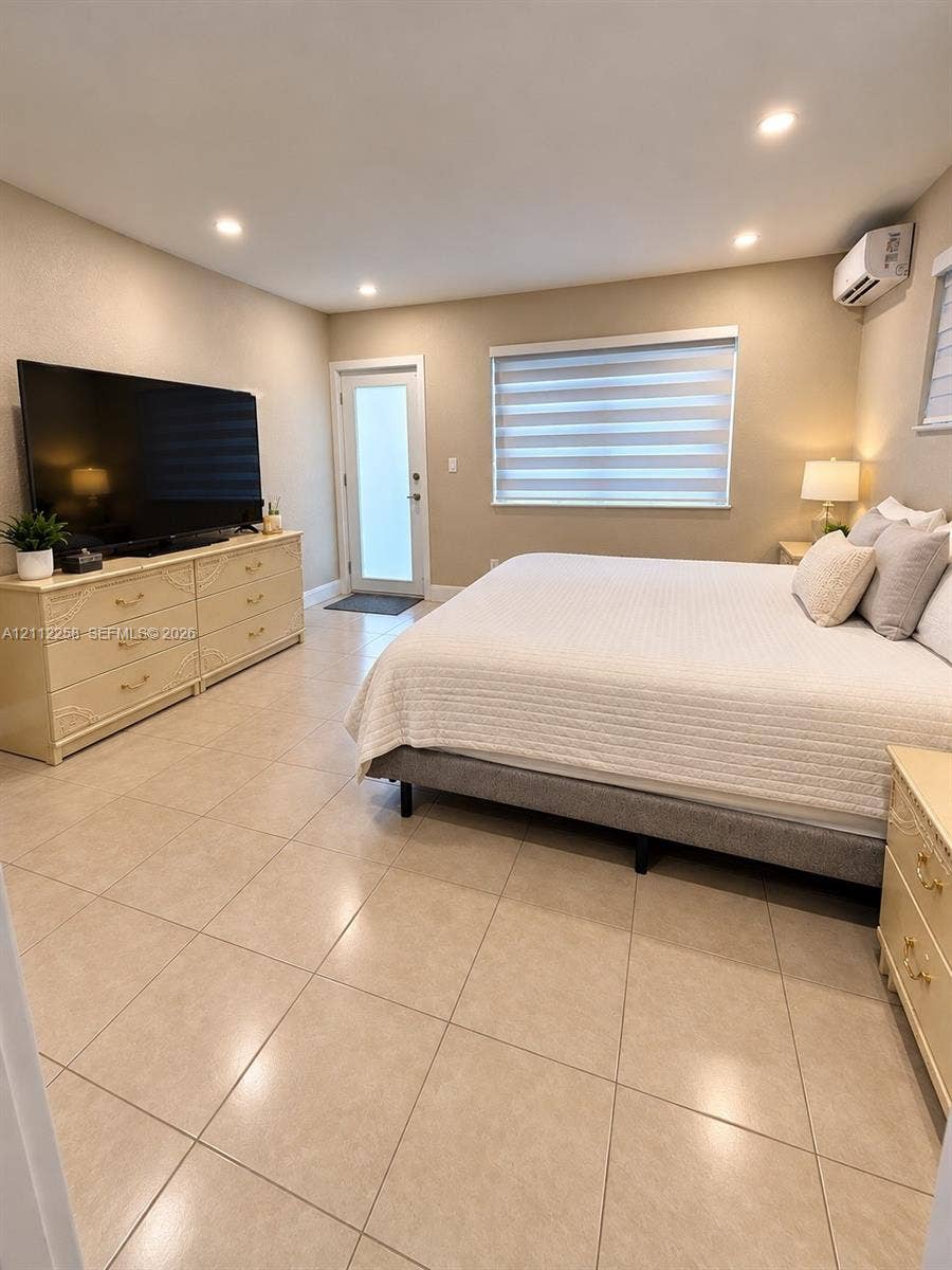 Neutral-toned ceramic tile flooring, recessed ceiling lighting, wall-mounted climate control unit, and window with adjustable light-filtering shade