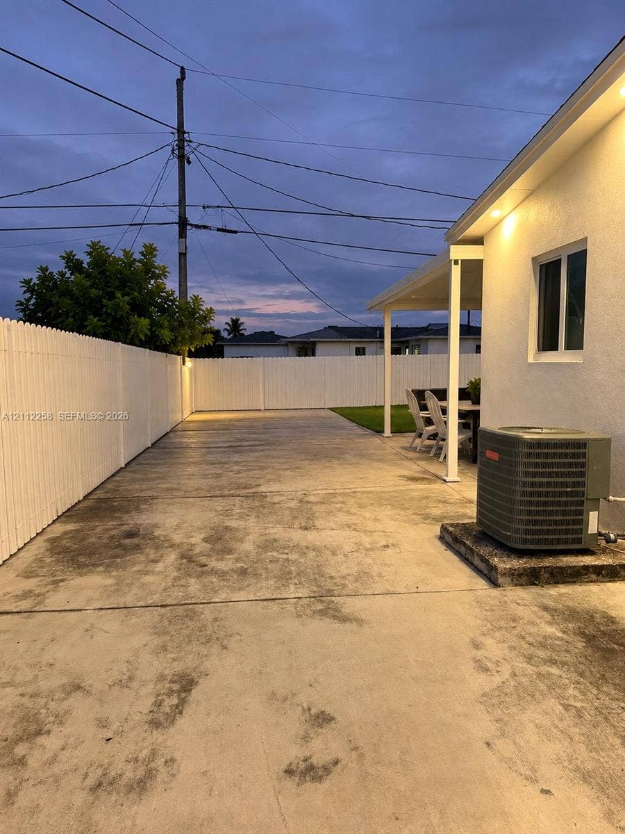 Concrete side patio featuring a covered overhang, enclosed by a white vinyl privacy fence with integrated recessed soffit lighting