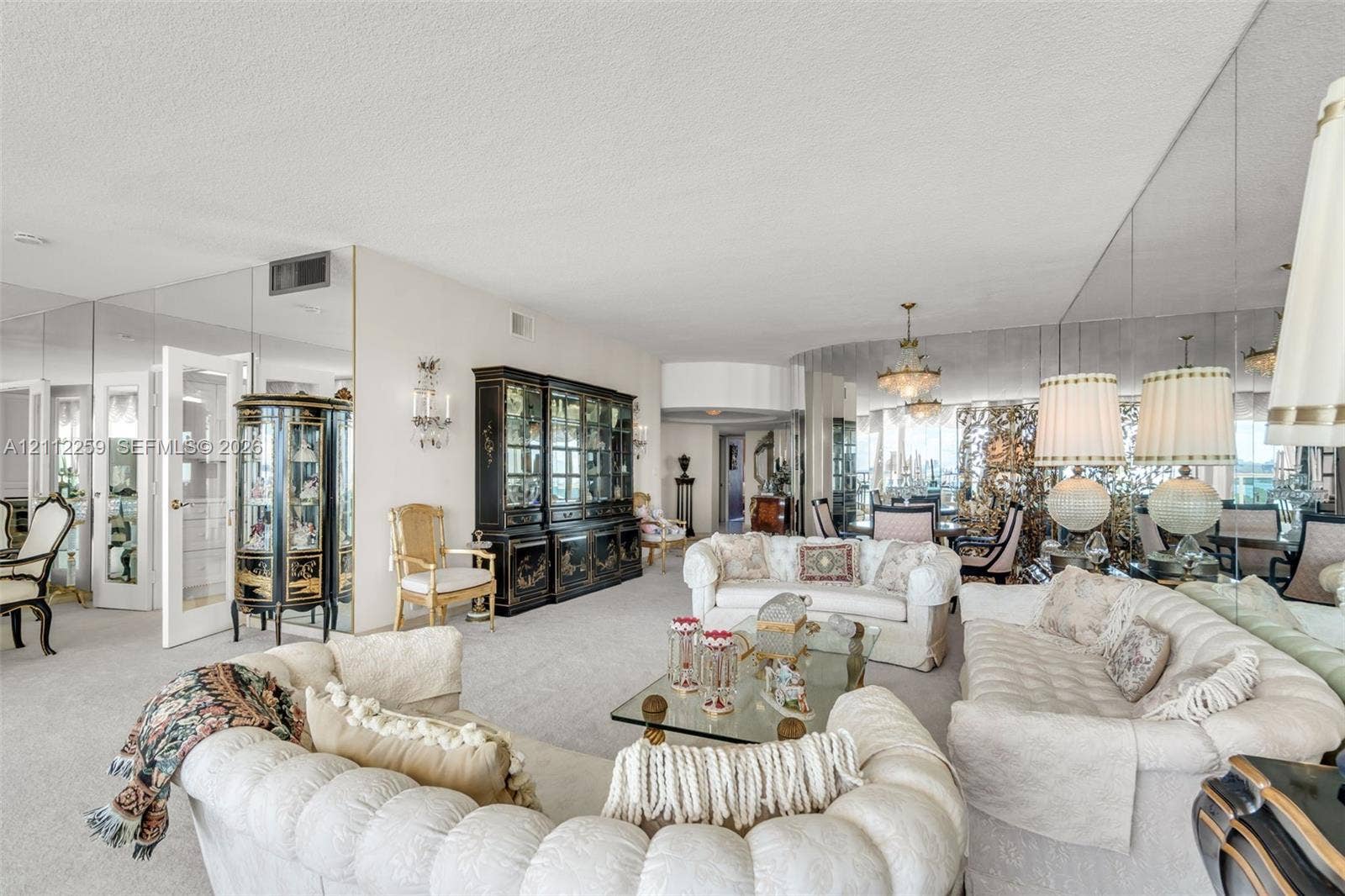 Expansive living space featuring wall-to-wall mirrored surfaces, a built-in floor-to-ceiling cabinet, dual multi-tiered chandeliers, and neutral wall-to-wall carpeting