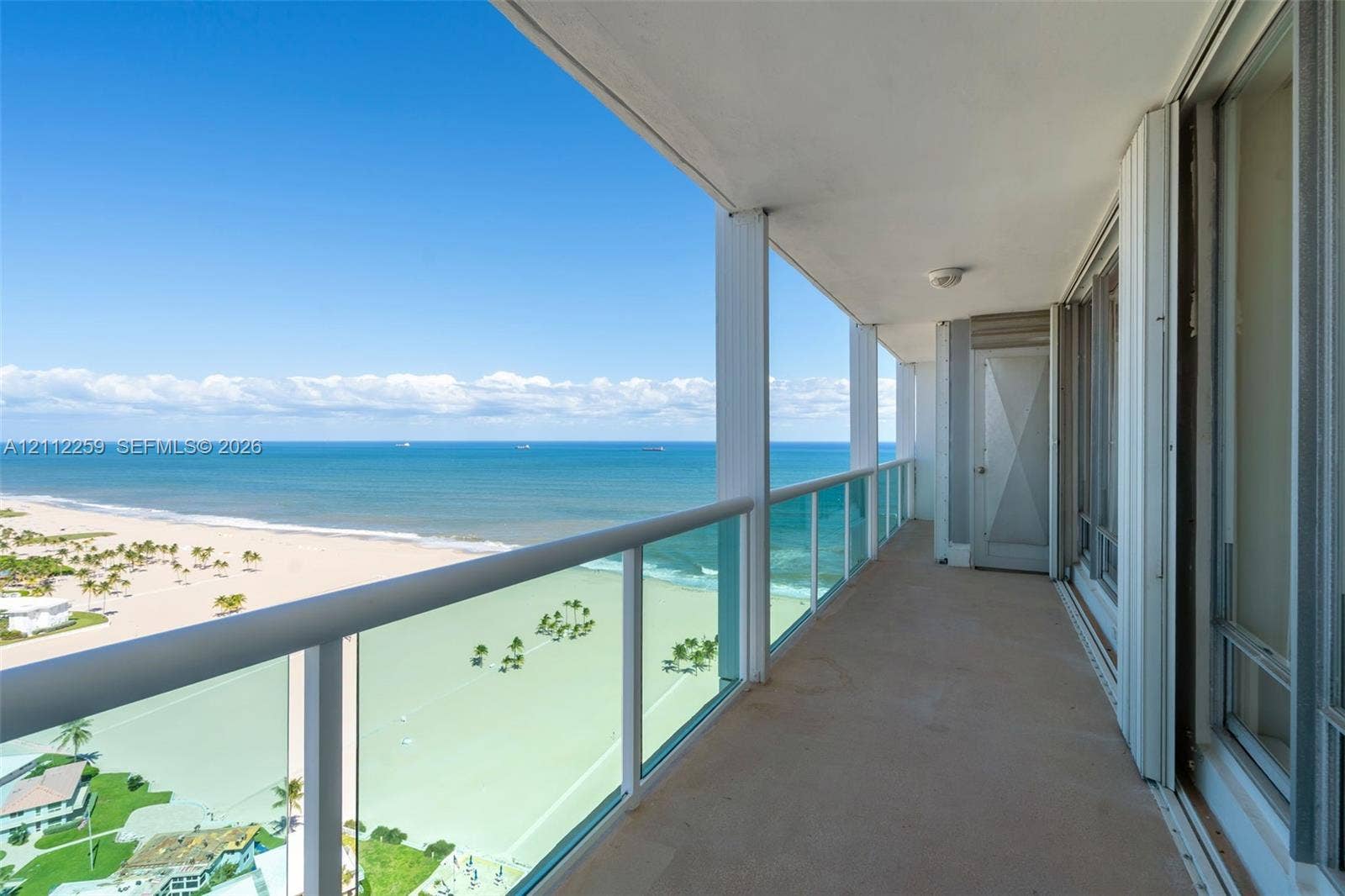 Covered balcony featuring glass-panel railings, solid surface flooring, and oceanfront exposure