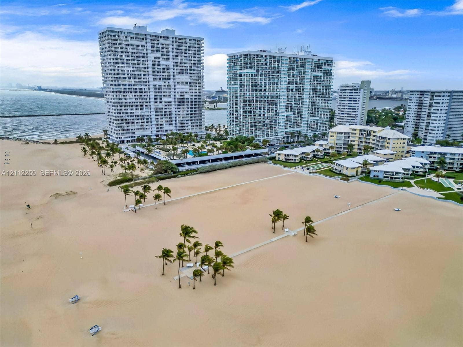 Direct oceanfront location featuring a sprawling sandy beach, clusters of mature palm trees, and elevated multi-story residential towers