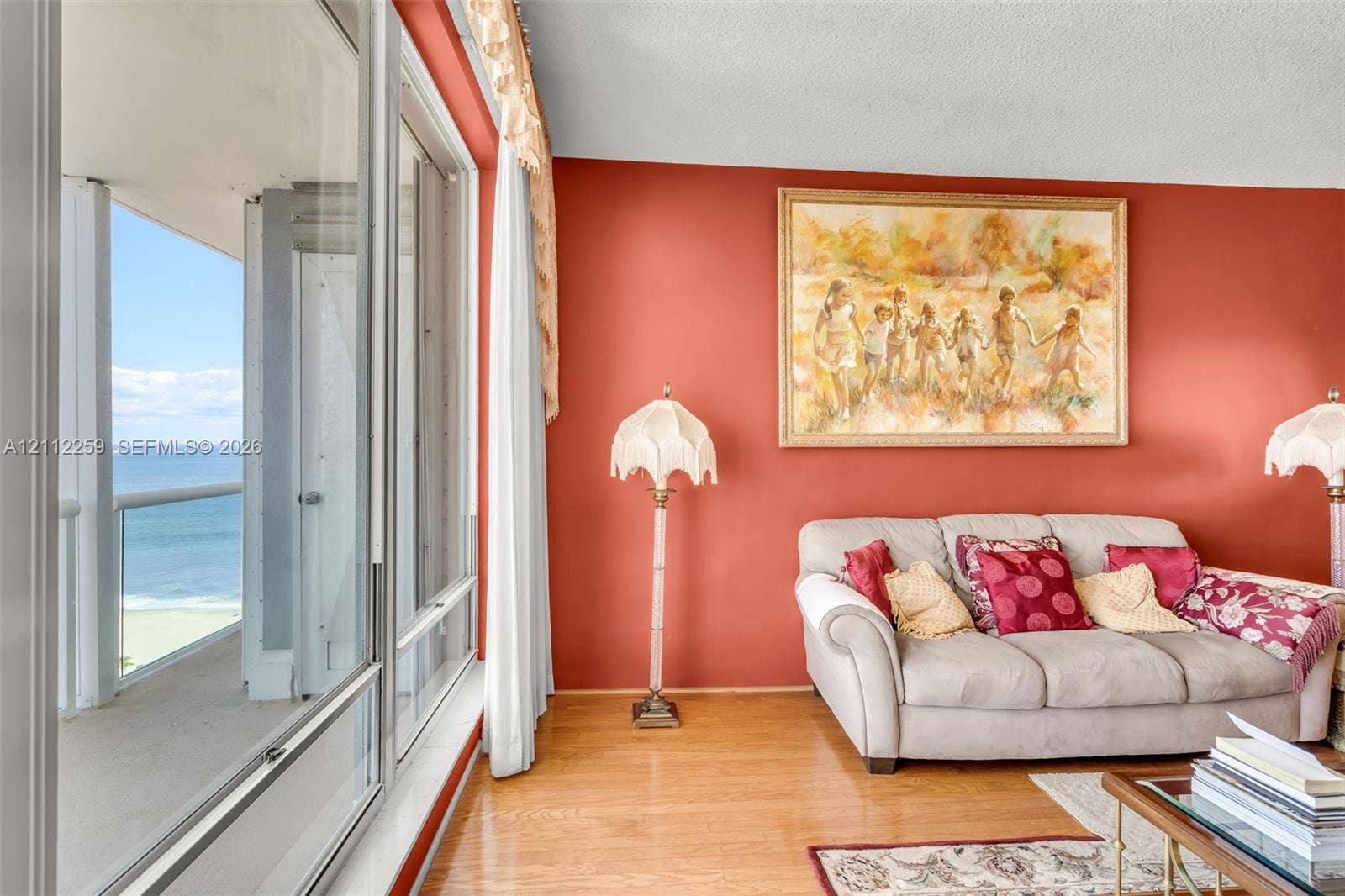 Floor-to-ceiling windows featuring ocean scenery, wood-finish flooring, and an attached balcony with a metal railing