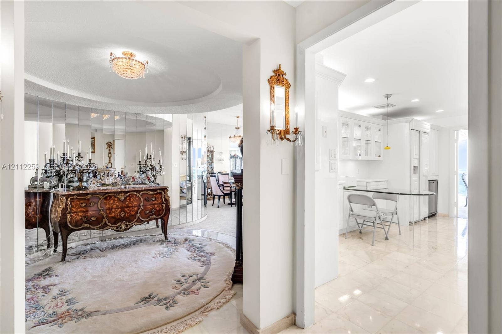 Foyer area featuring recessed tray ceiling, polished tile flooring, mirrored wall accents, and ornamental wall-mounted light fixtures
