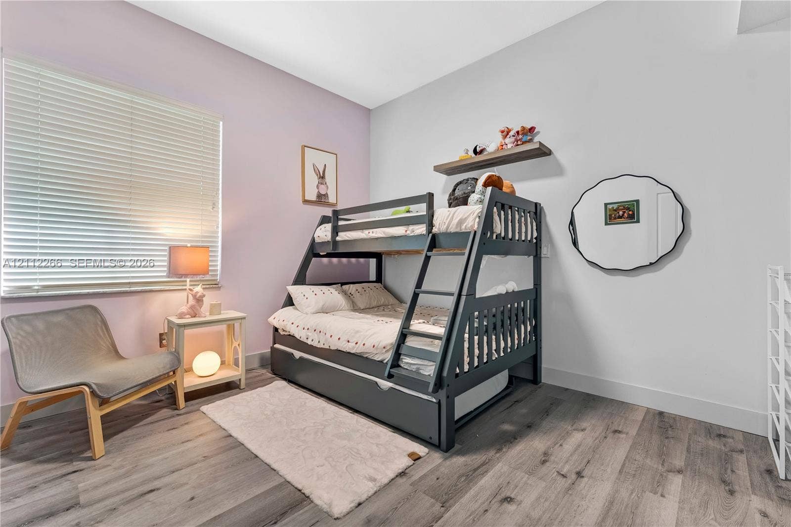 Neutral-toned room featuring wood-finish flooring, a wall-mounted floating shelf, and a window with horizontal blinds